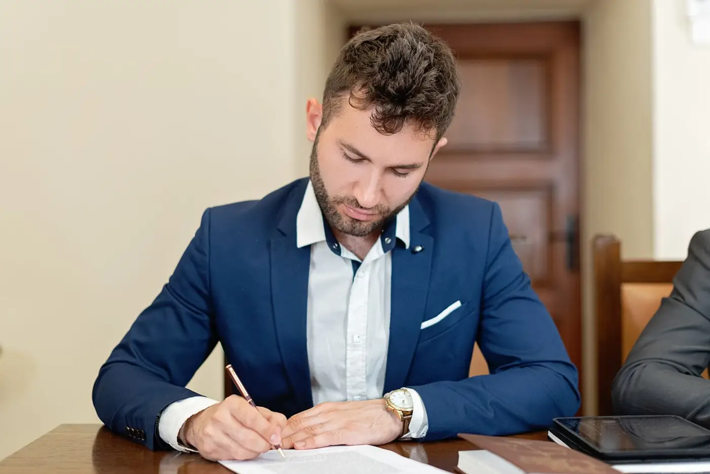 One and the Same Person Affidavit, How It Works in Dubai 5 A young man in a blue blazer signing a document at a wooden table