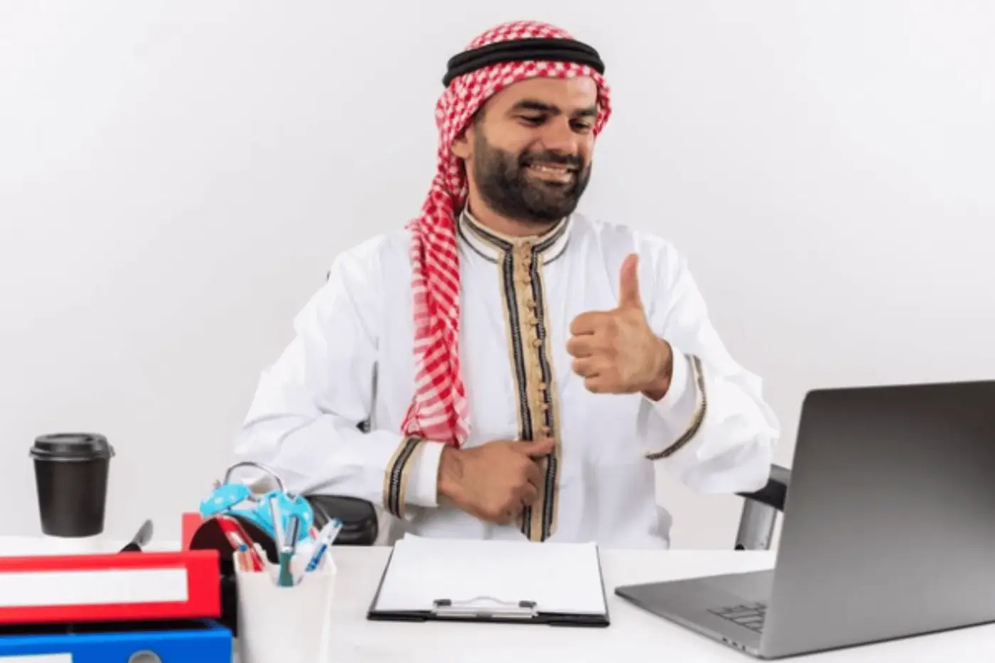 A smiling man at a desk with a laptop and paperwork