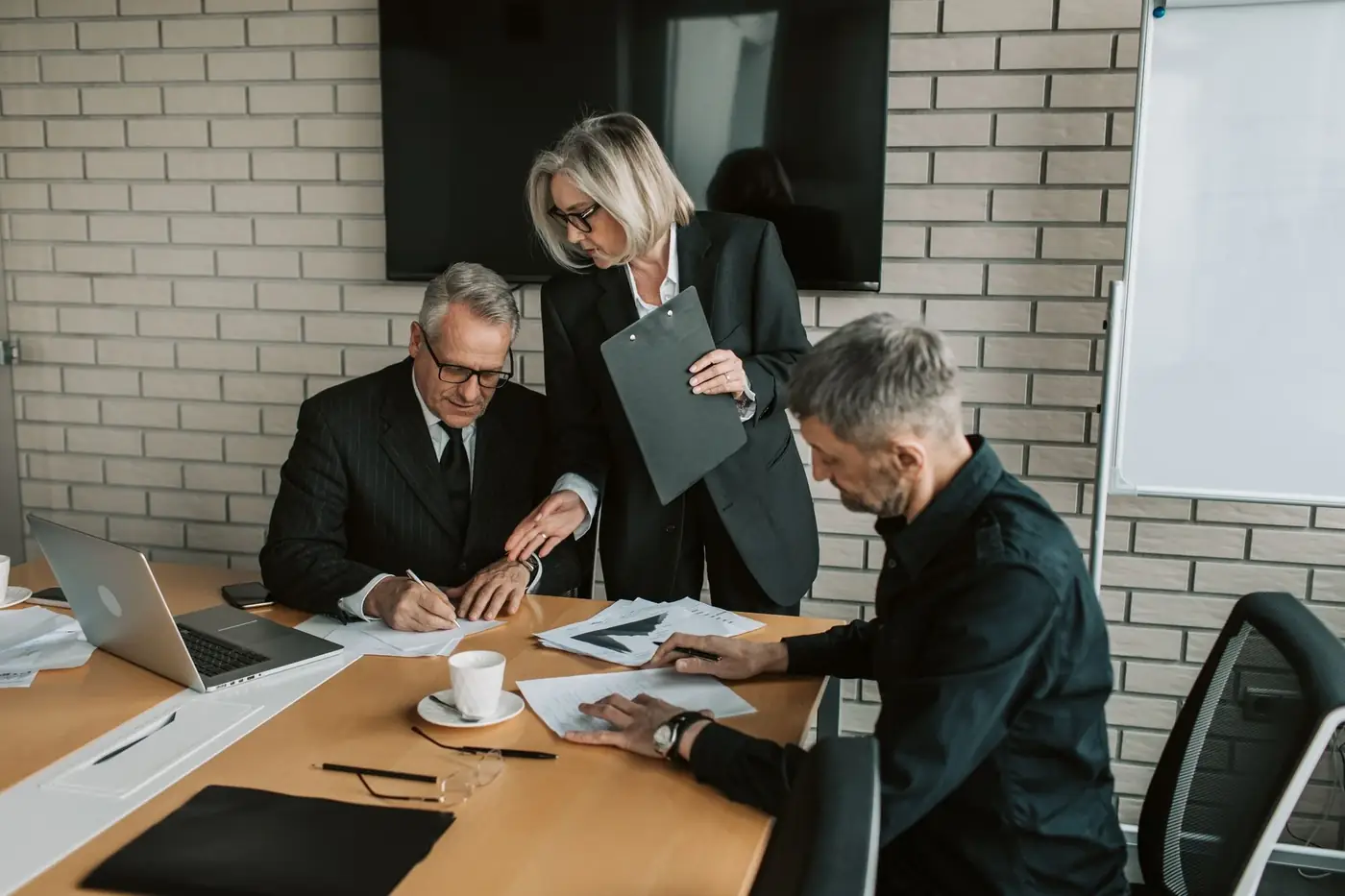 Corporate and Business Notary Services in Dubai 80 A director signing papers at a boardroom table beside two colleagues