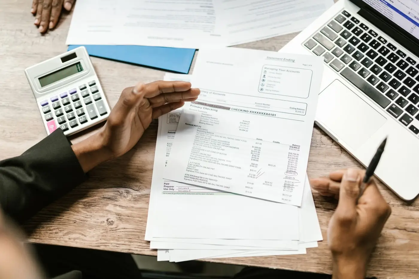 Certified True Copy Attestation in Sharjah 4 Two people reviewing a printed bank statement beside a calculator and laptop