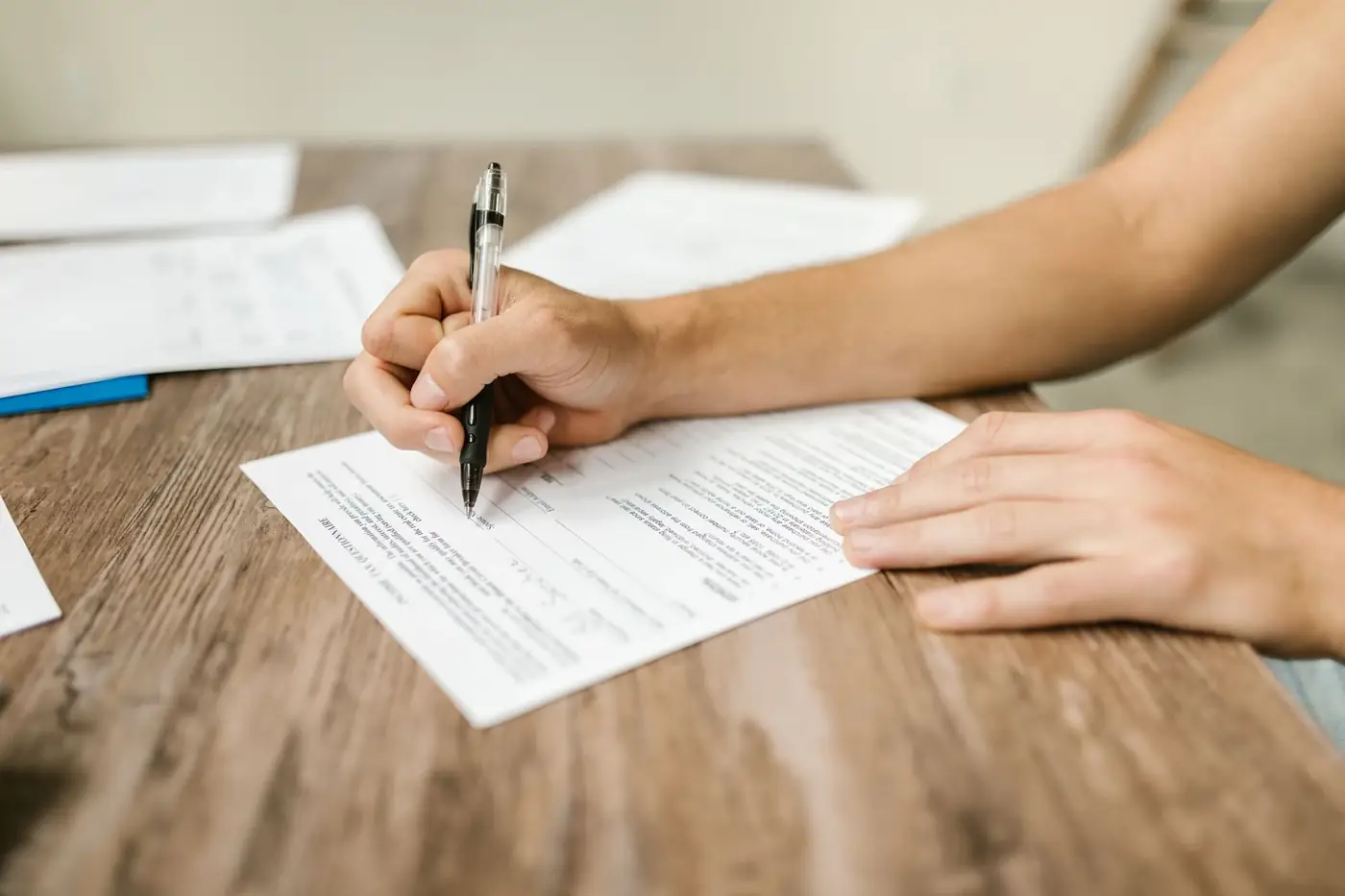 Declaration of Unemployment in the UAE 1 A person filling in a printed form with a pen at a wooden table