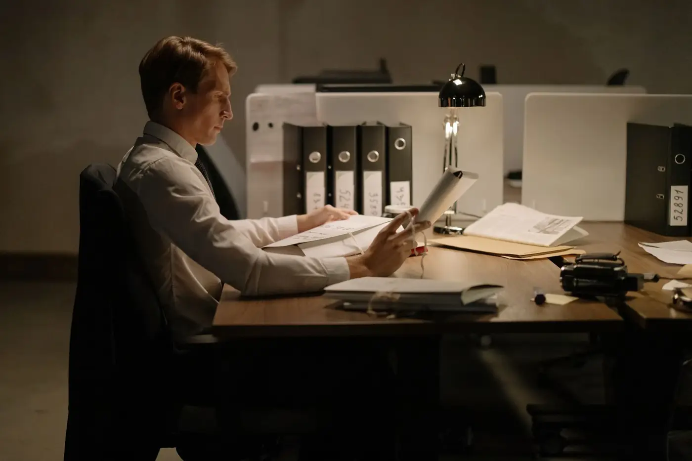 A man reading papers at his desk under a lamp at night