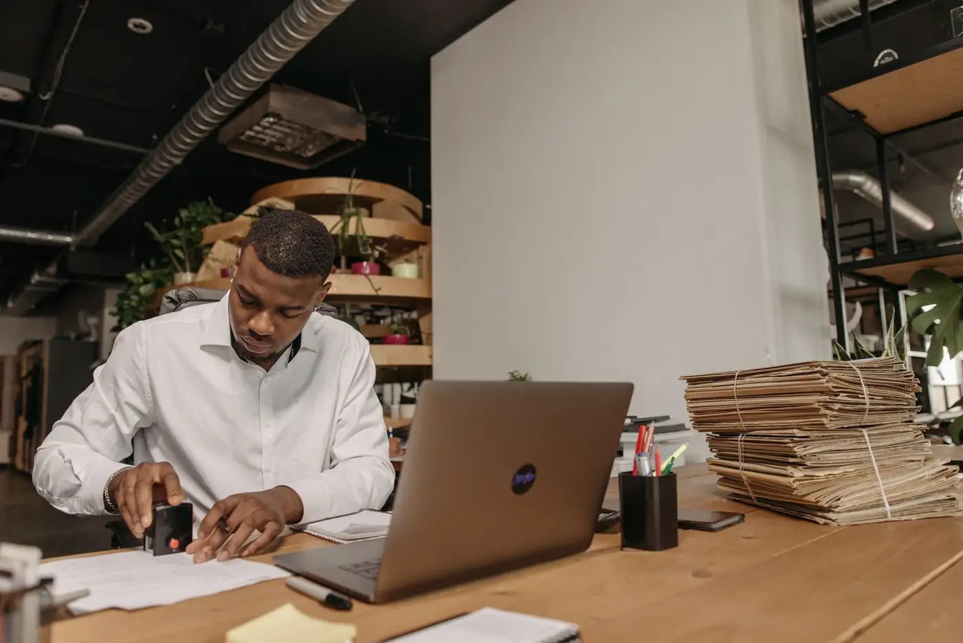 A man in a white shirt stamping papers at a wooden office desk