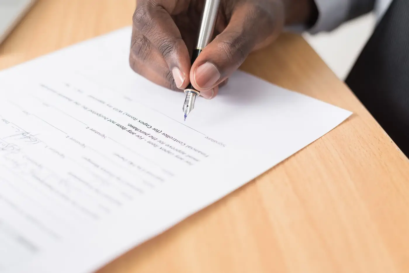 Hand signing a single printed document with a fountain pen on a desk