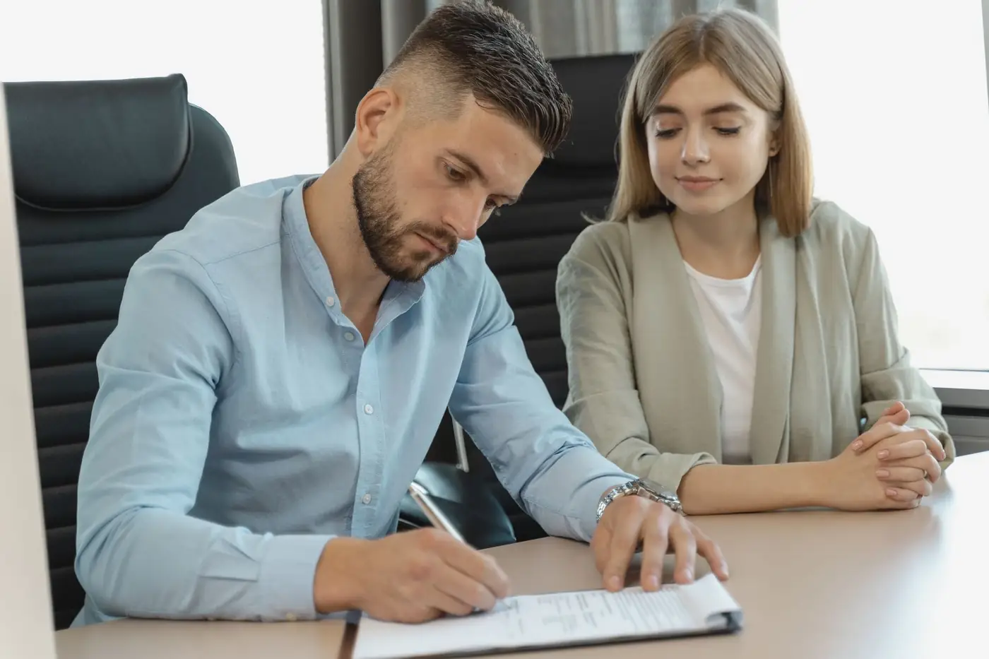 Notary Attestation Services in Abu Dhabi 1 A man signing a document at an office desk while a woman watches