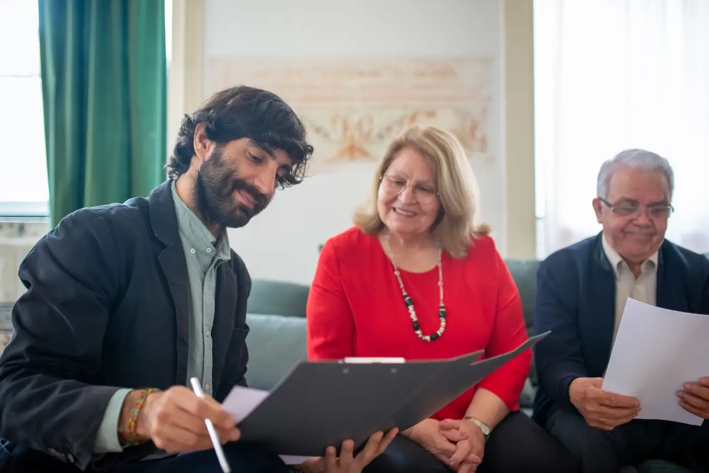 How to notarise a document in Dubai, step by step 4 A man signing papers on a clipboard with an older couple on their sofa