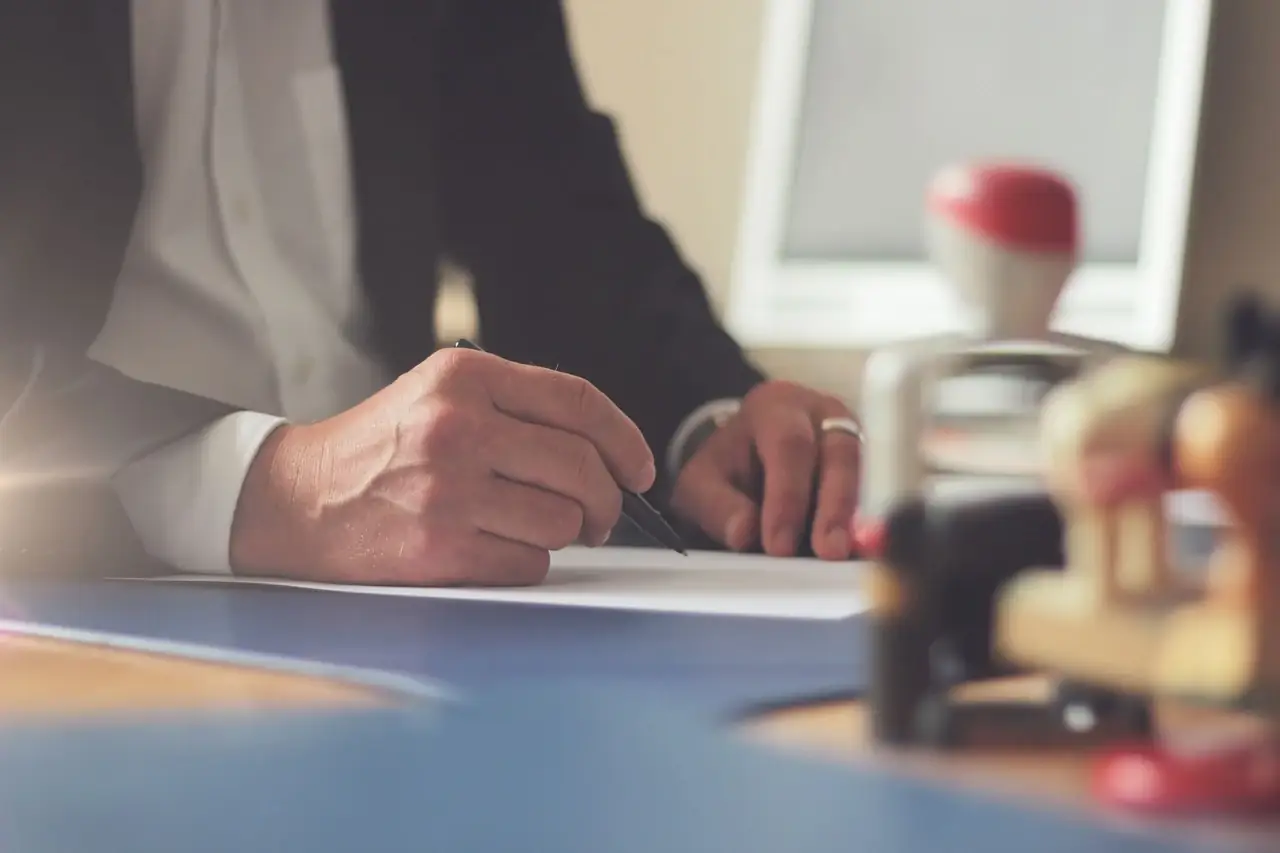 Our legal documentation services in Dubai 1 A man in a suit signing a document behind a row of office stamps
