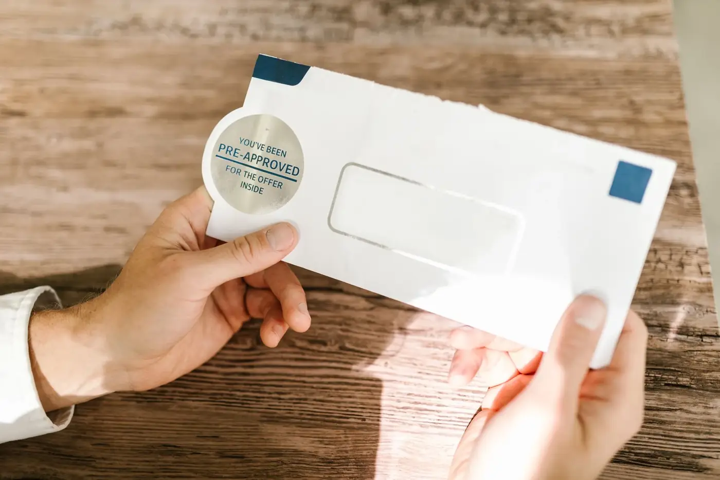 Hands holding an opened window envelope over a wooden table