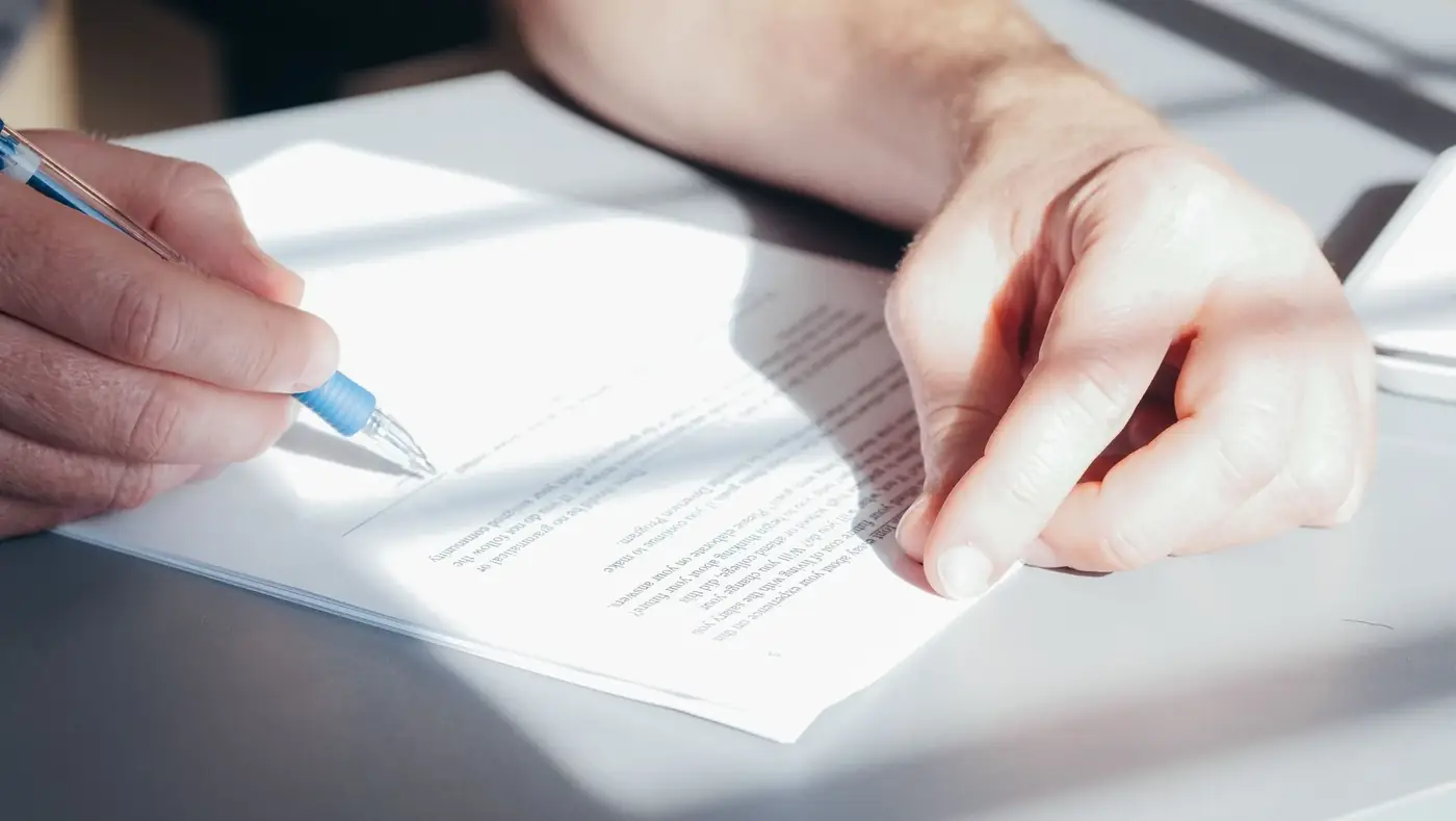 Close view of a hand signing a single printed page with a blue pen