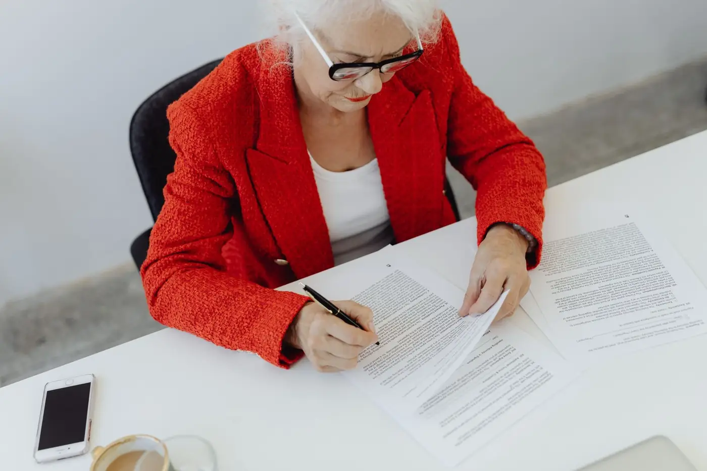 Notary for a Will in Dubai: Making and Registering Your Will 1 An older woman in a red jacket signing papers at a white desk