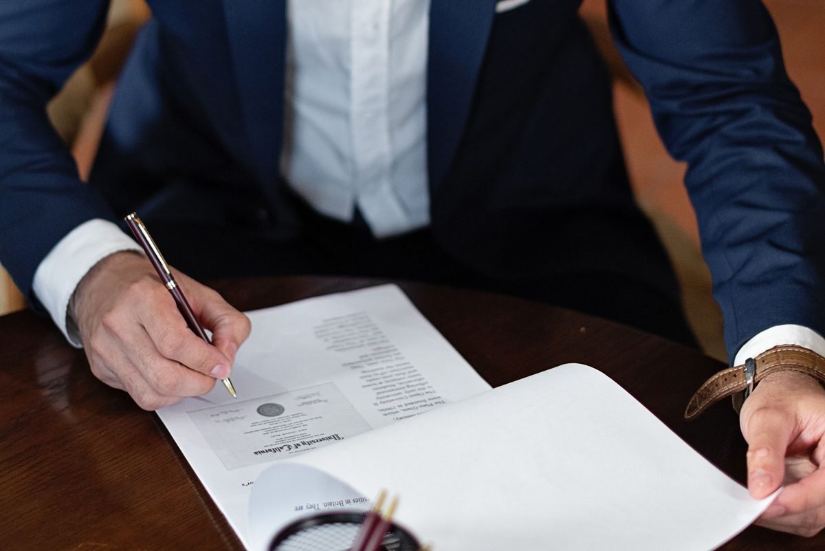 Man in a navy suit signing a document at a desk before notarization